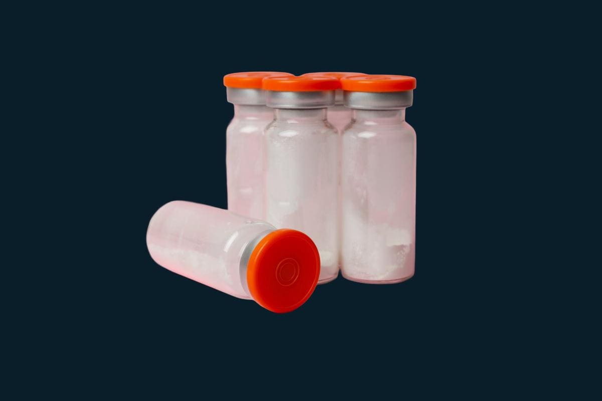 Four glass vials of white lyophilized powder with orange caps, one lying on its side